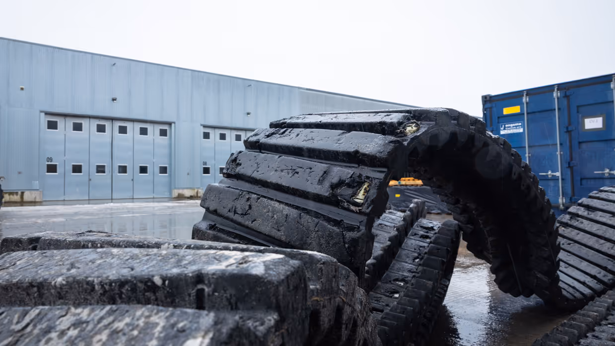 Links: een versleten rubberen band track, rechts: met een heftruck wordt een rubberen band track omhoog gehesen.