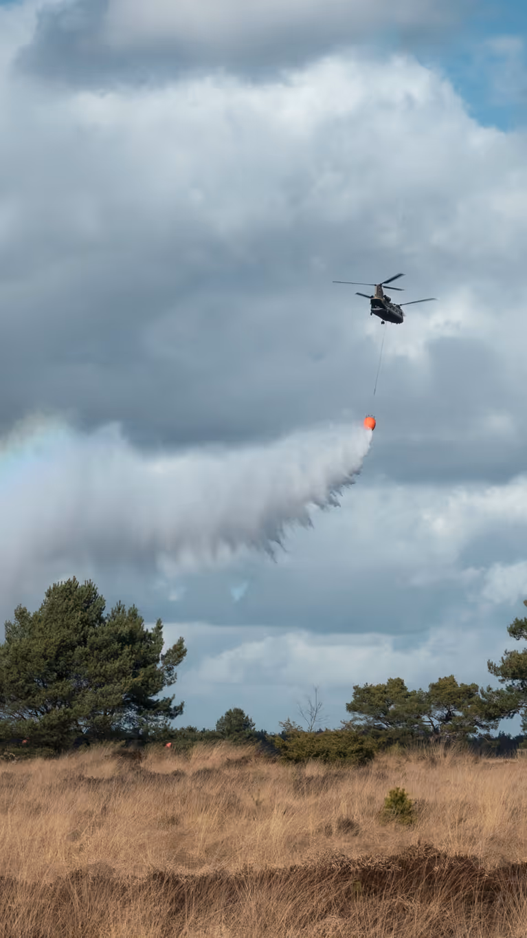 Een helikopter dropt water boven de hei. In de waternevel ontstaat een regenboog.