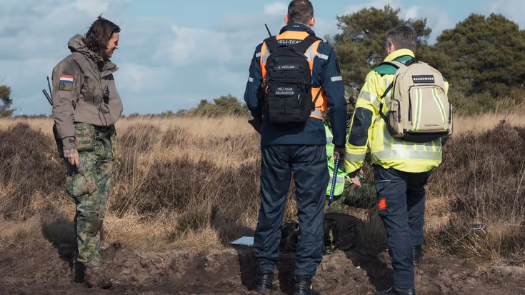 Een militair en twee brandweermannen overleggen op de hei.