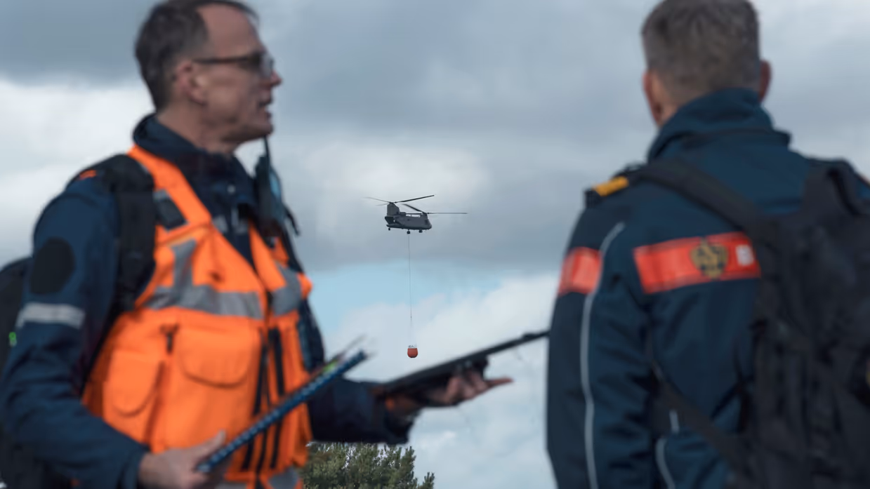 Twee personen overleggen op een militair oefenterrein.