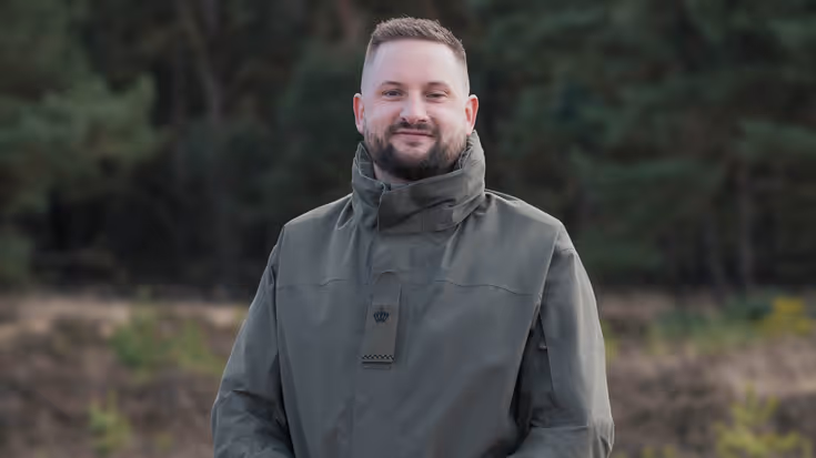 Een militair poseert met handen over elkaar op de hei.