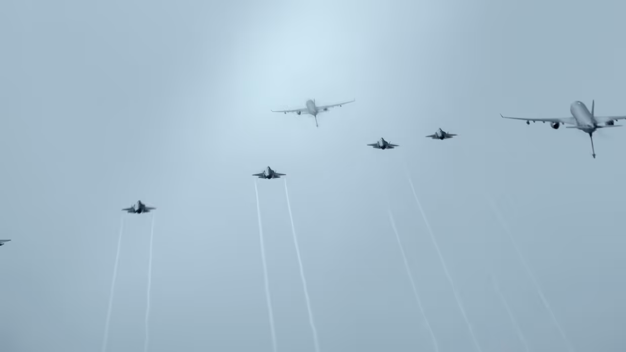Bovenaanzicht van twee A330 MRTT’s en vijf F-35’s die tegen een egaal grijs wolkendek vliegen.