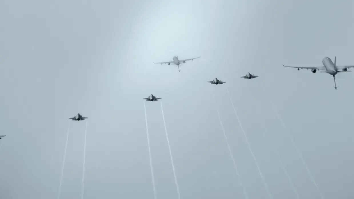Bovenaanzicht van twee A330 MRTT’s en vijf F-35’s die tegen een egaal grijs wolkendek vliegen.