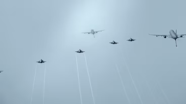 Bovenaanzicht van twee A330 MRTT’s en vijf F-35’s die tegen een egaal grijs wolkendek vliegen.