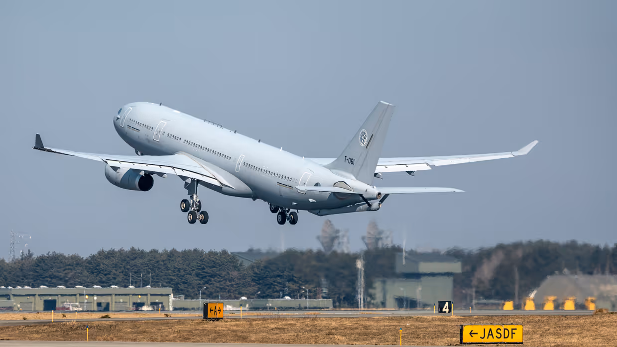 Een A330 MRTT stijgt op. In de achtergrond zijn hangars en radartorens te zien.