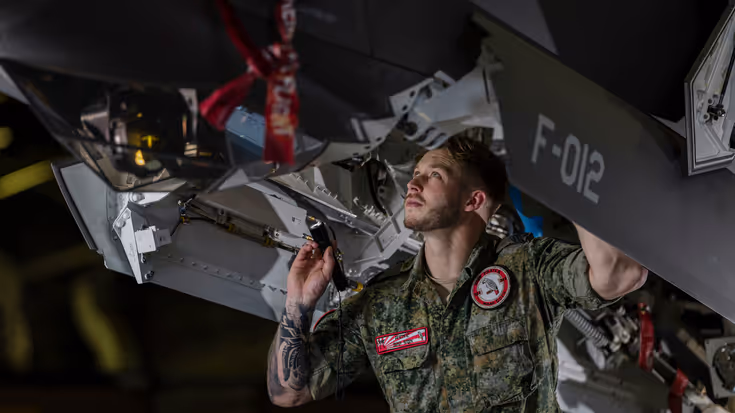 Een militair in groen camouflagepak inspecteert het neuswiel van een F-35/kijkt op een laptop.