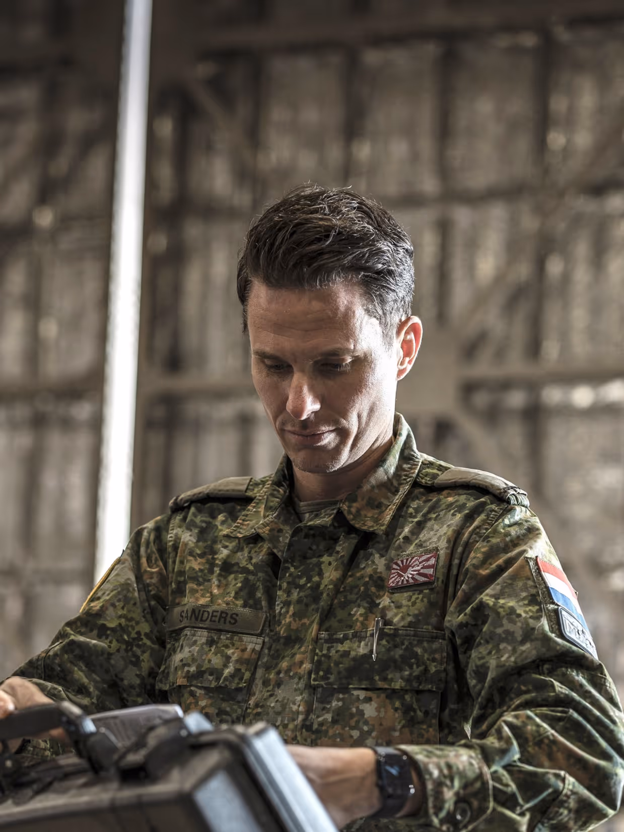 Een militair in een groen camouflagepak bekijkt een koffer die hij uit een container pakt.