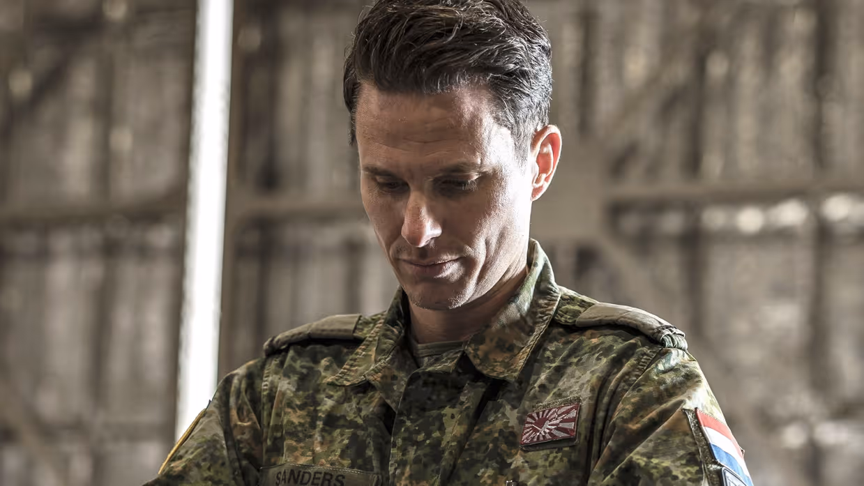 Een militair in een groen camouflagepak bekijkt een koffer die hij uit een container pakt.