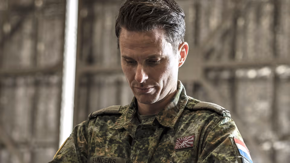 Een militair in een groen camouflagepak bekijkt een koffer die hij uit een container pakt.