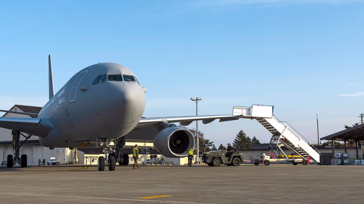 Een groene tow truck rijdt met een grote vliegtuigtrap naar een A330 MRRT die links in beeld staat.