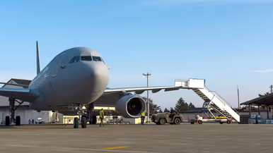 Een groene tow truck rijdt met een grote vliegtuigtrap naar een A330 MRRT die links in beeld staat.