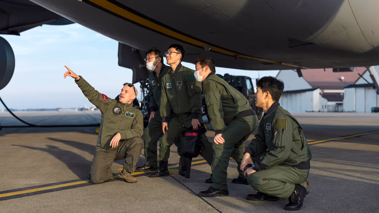 Een groep Japanse militairen knielt en staat gebogen onder de romp van een A330 MRTT en kijkt en wijst naar boven.