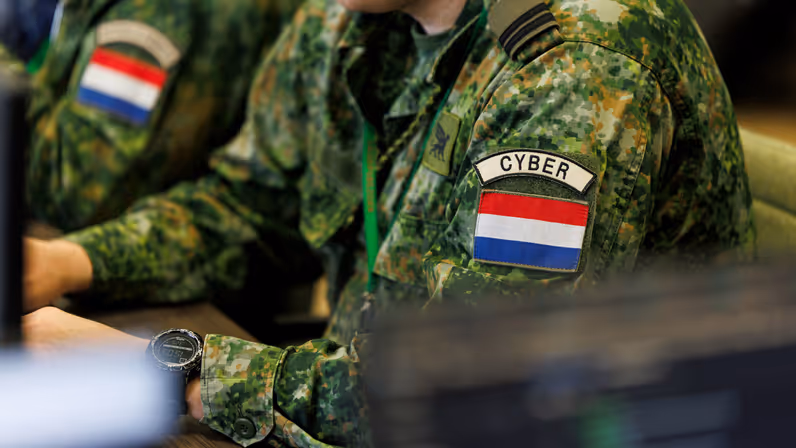 Militair met een cyber patch op zijn linkerarm aan het werk achter een computer.&nbsp;