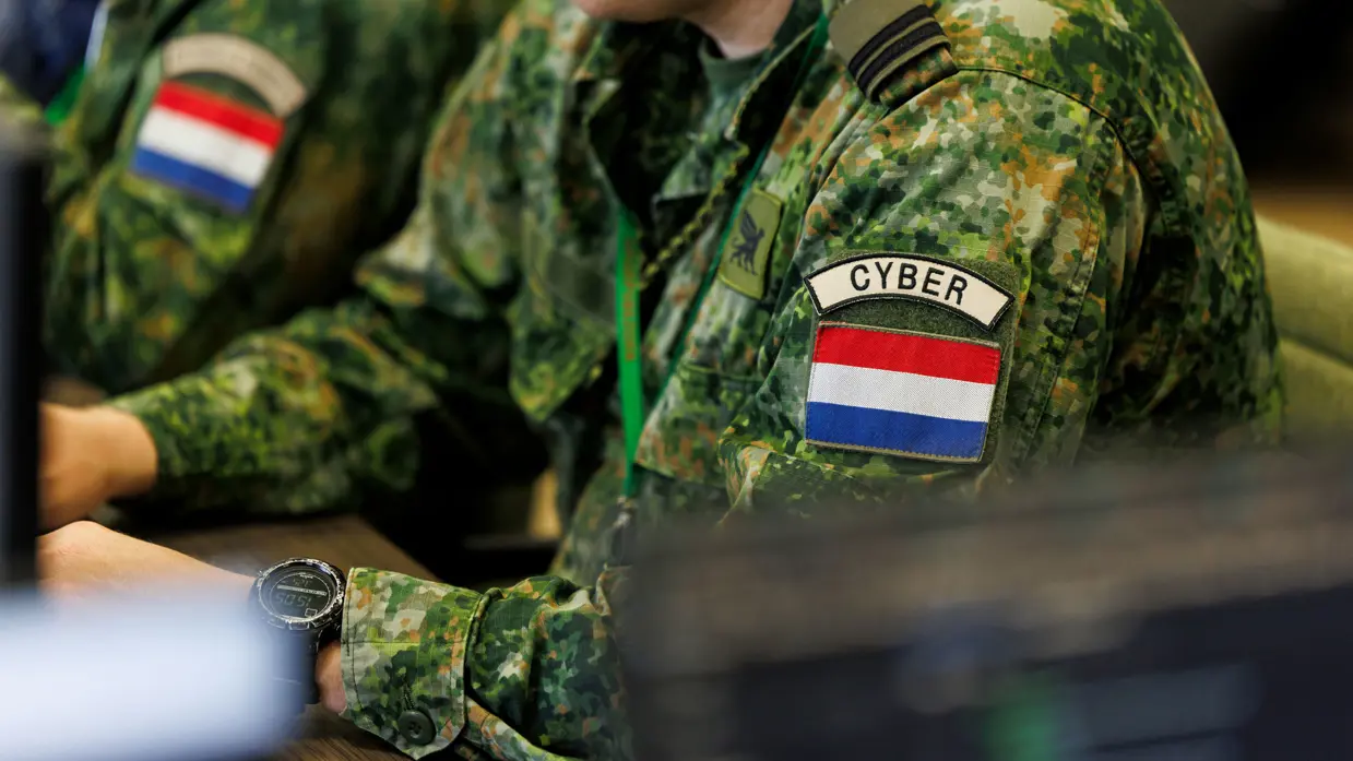 Militair met een cyber patch op zijn linkerarm aan het werk achter een computer.&nbsp;
