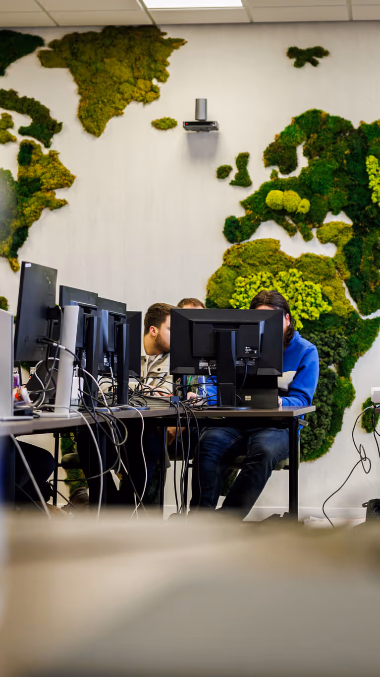 Werkende mensen achter computers met een wereldkaart van mos op de achtergrond. 