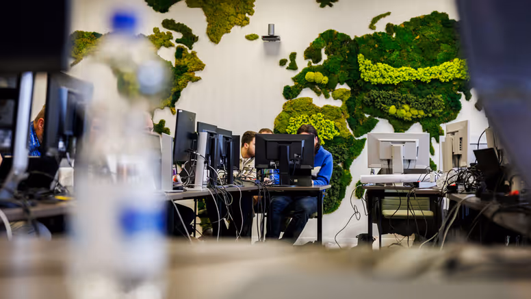 Werkende mensen achter computers met een wereldkaart van mos op de achtergrond. 