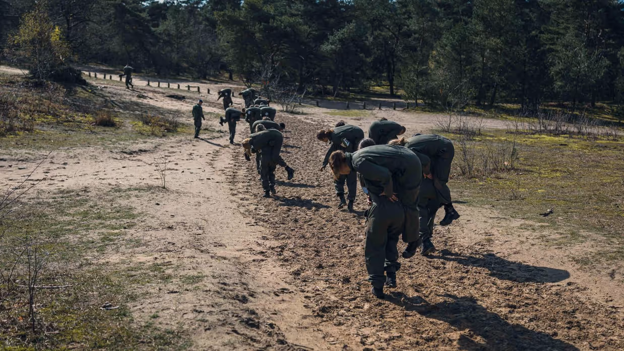 Meer dan 10 militairen rennen over de heide met een collega in de brandweergreep.