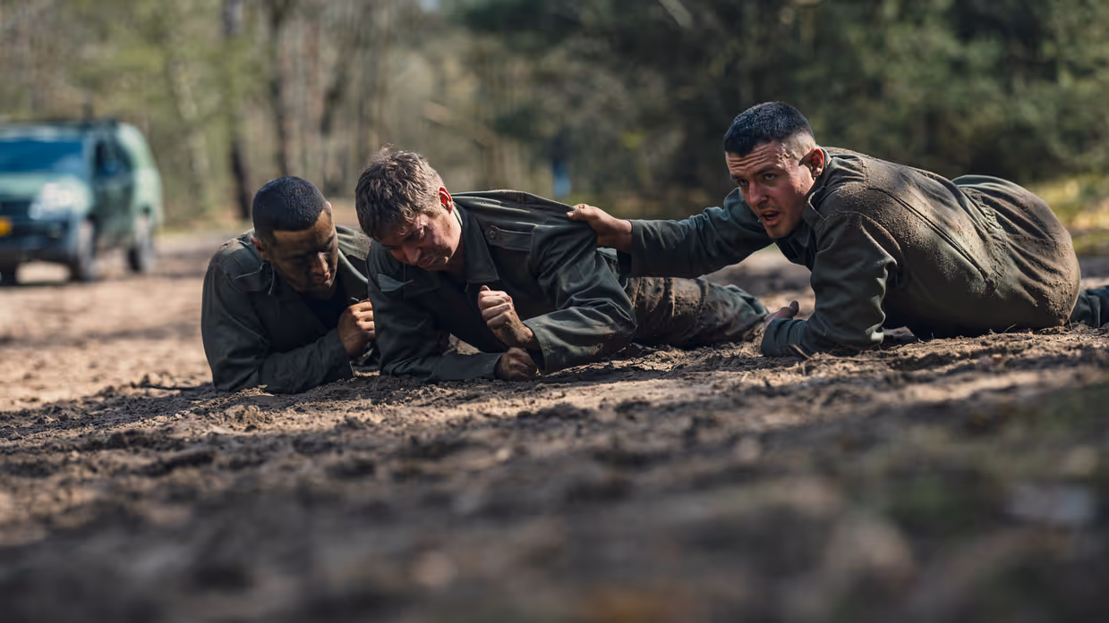 Een cadet liggend op de grond wordt vastgepakt en begeleid door 2 collega’s.