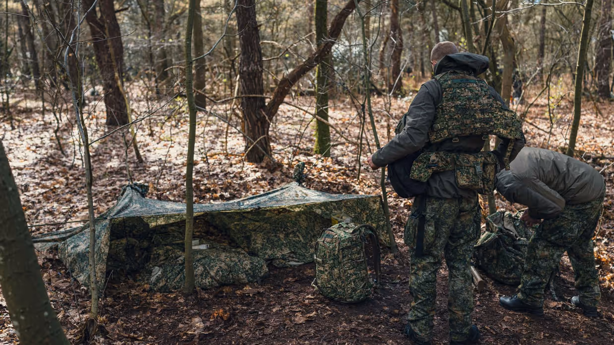 2 militairen ontfermen zich over 2 rugzakken voor een camouflagetentje.