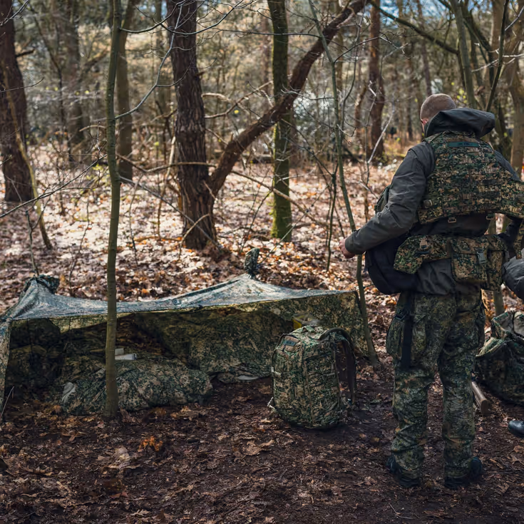 2 militairen ontfermen zich over 2 rugzakken voor een camouflagetentje.