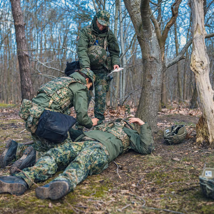 2 militairen ontfermen zich over een gewonde collega op de grond.