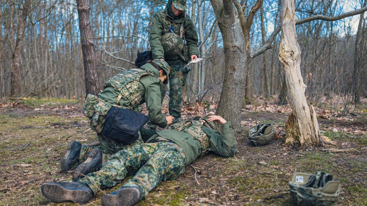 2 militairen ontfermen zich over een gewonde collega op de grond.