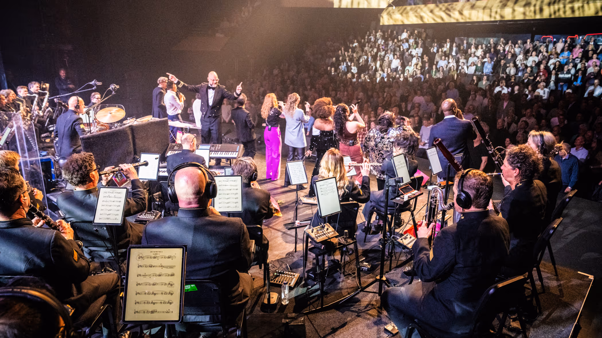 Het Luchtmachtorkest treedt op met zangers voor een volle zaal.