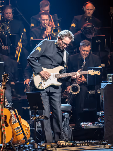 De slaggitarist tijdens een gitaarsolo. In de achtergrond kijken collega-musici toe.