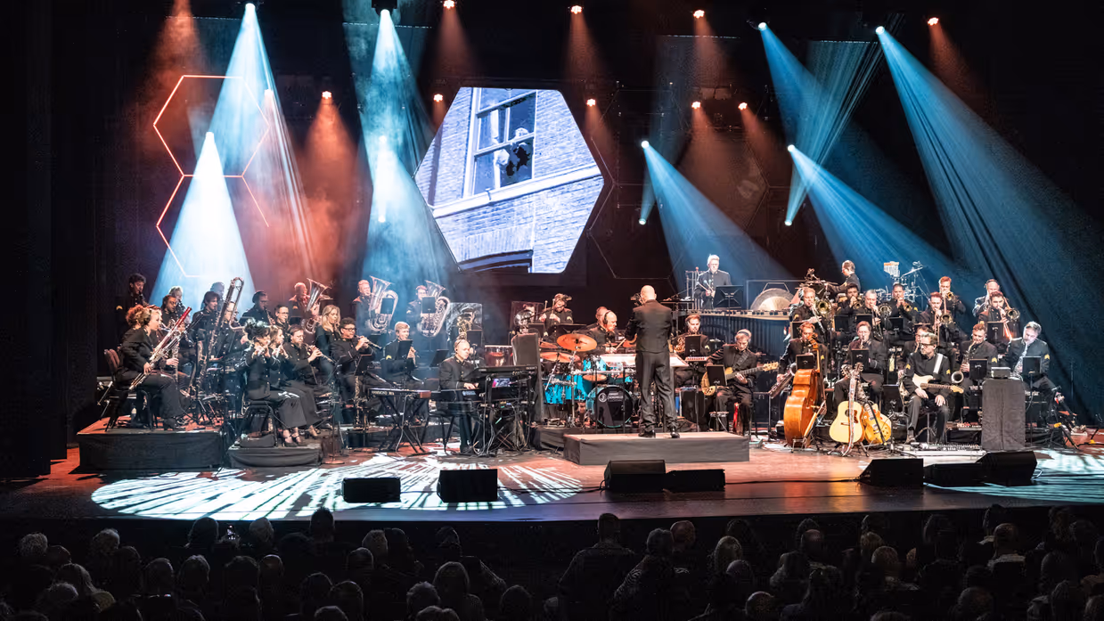 Orkest Koninklijke Luchtmacht tijdens een concert met dirigent en lichtshow op het podium.