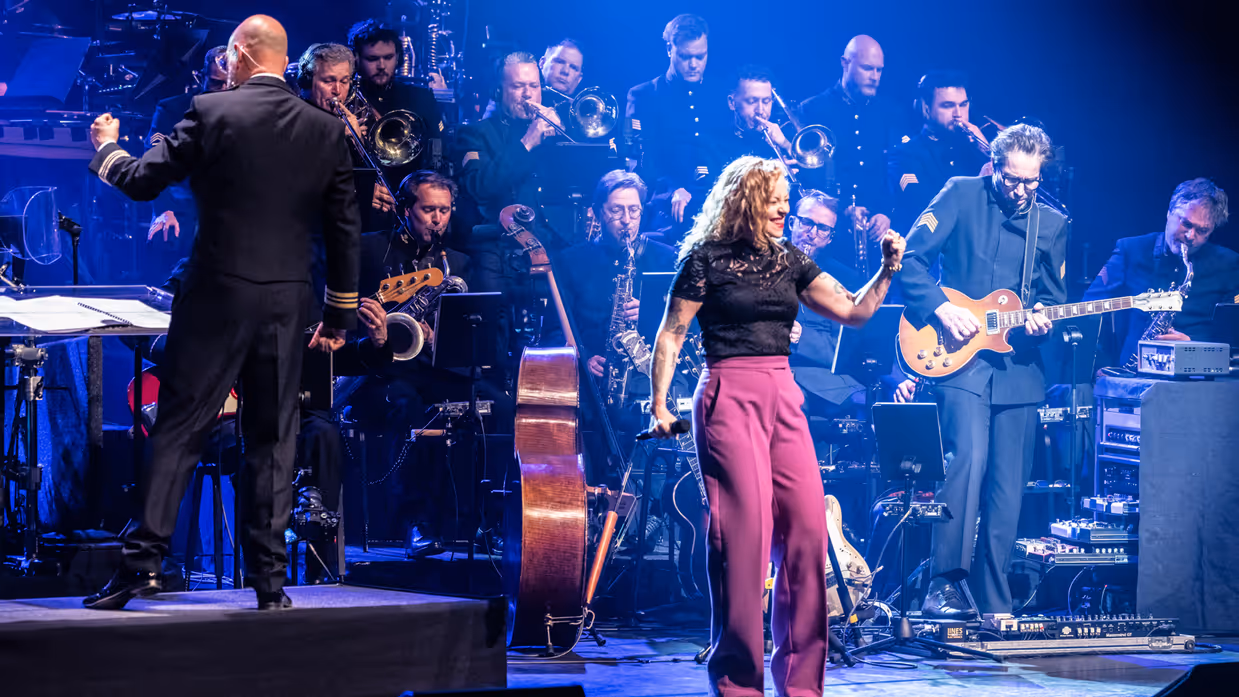 Anneke van Giersbergen danst voor op het podium. In de achtergrond speelt een deel van het orkest. Links de dirigent.