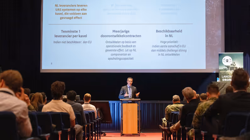 Presentatie over drones en UAS-systemen voor een publiek in een zaal. 