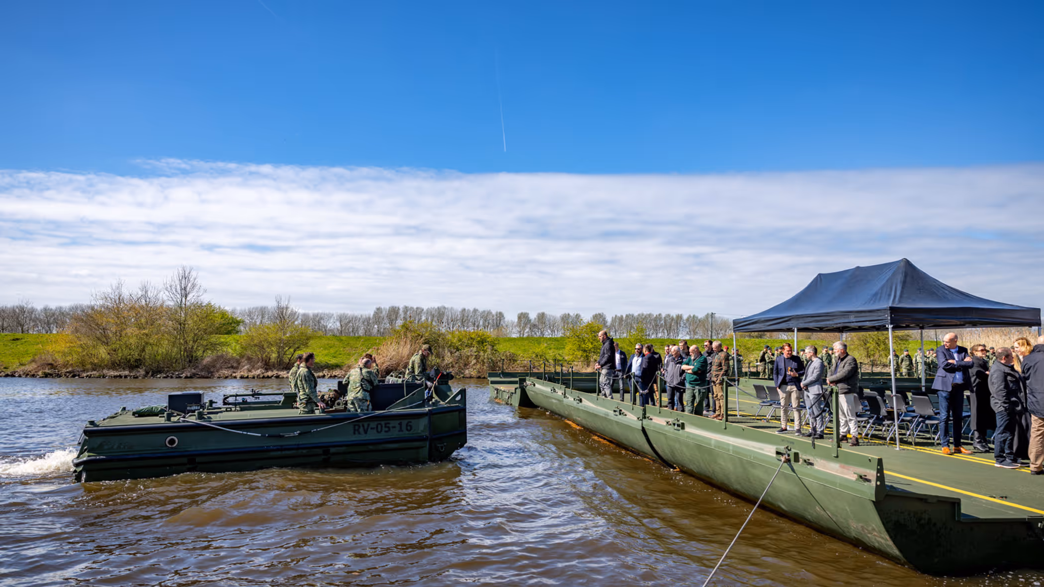Nieuwe brugslagcapaciteit ligt over een rivier. Daarnaast vaart een boot met militairen. 