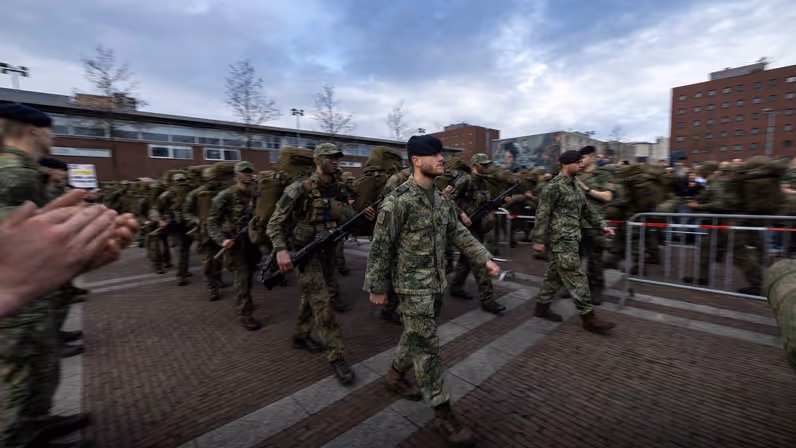 De nieuwe mariniers met rugzak en wapen lopen in het gelid het kazerneterrein op, tussen applaudisserende collega’s door.&nbsp;
