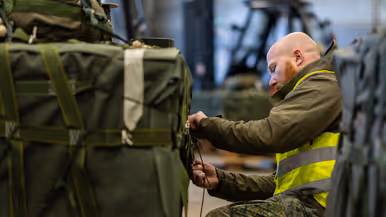 Een militair is bezig met het insnoeren van een groene vrachtbundel.