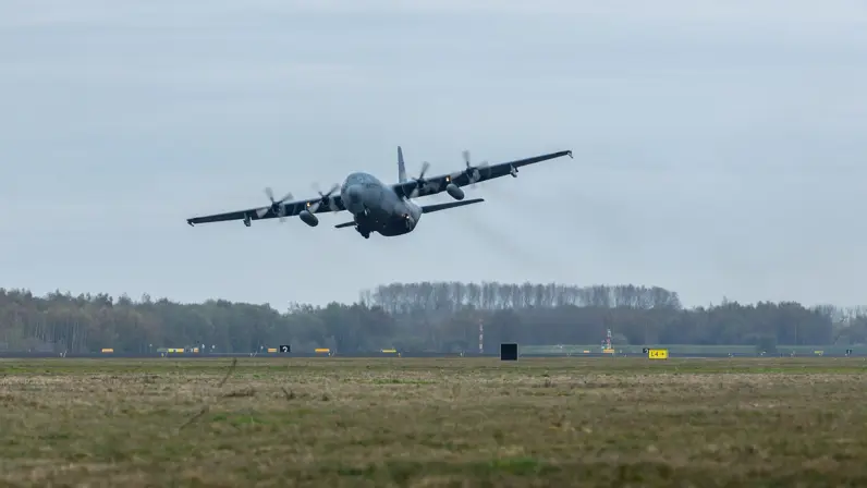 Een transportvliegtuig stijgt op, het landingsgestel is nog nét uitgeklapt.