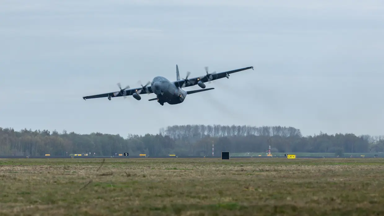 Een transportvliegtuig stijgt op, het landingsgestel is nog nét uitgeklapt.