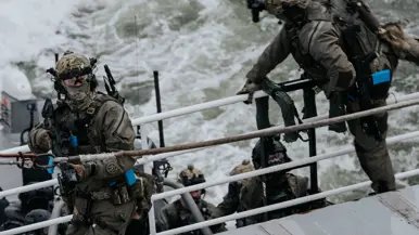 Op de linkerfoto klimt een militair aan boord, terwijl een collega dekking geeft. Rechts hangt een blauwe politiehelikopter stil boven het schip om operators af te zetten aan boord.