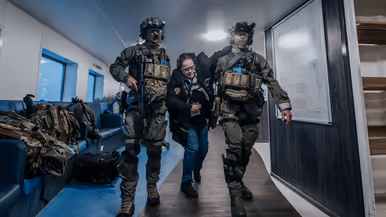 Links controleert een NLMARSOF-militair een vrouw die bleek ziet en duidelijk in nood verkeert. Rechts ondersteunen 2 gewapende NLMARSOF-operators een gewonde dame. Ze lopen over een scheepsdek.