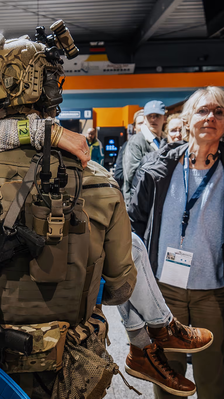 Een operator van NLMARSOF draagt een vrouw in zijn armen. Hij loopt een terminal binnen waar ook andere passagiers worden opgevangen.