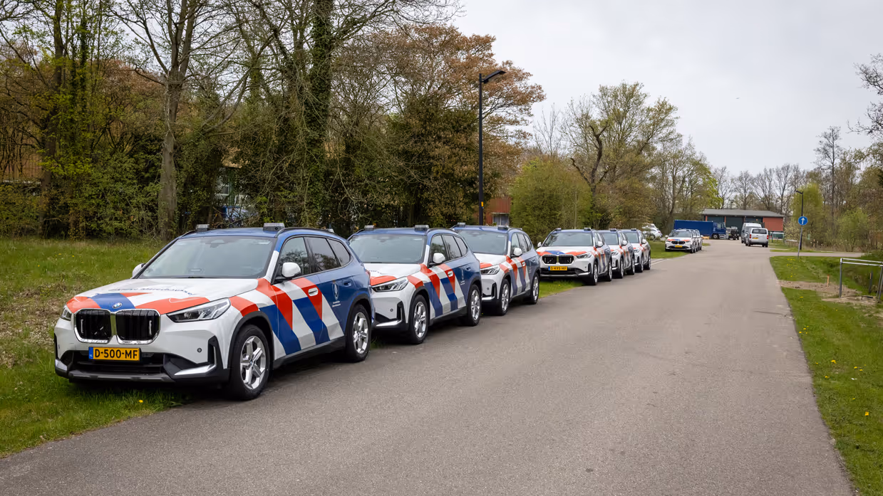 Voertuigen Marechaussee staan achter elkaar in de berm geparkeerd.