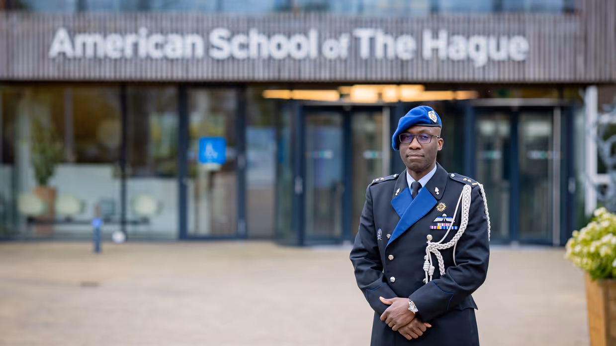 Marechaussee in uniform staat voor ingang schoolgebouw.