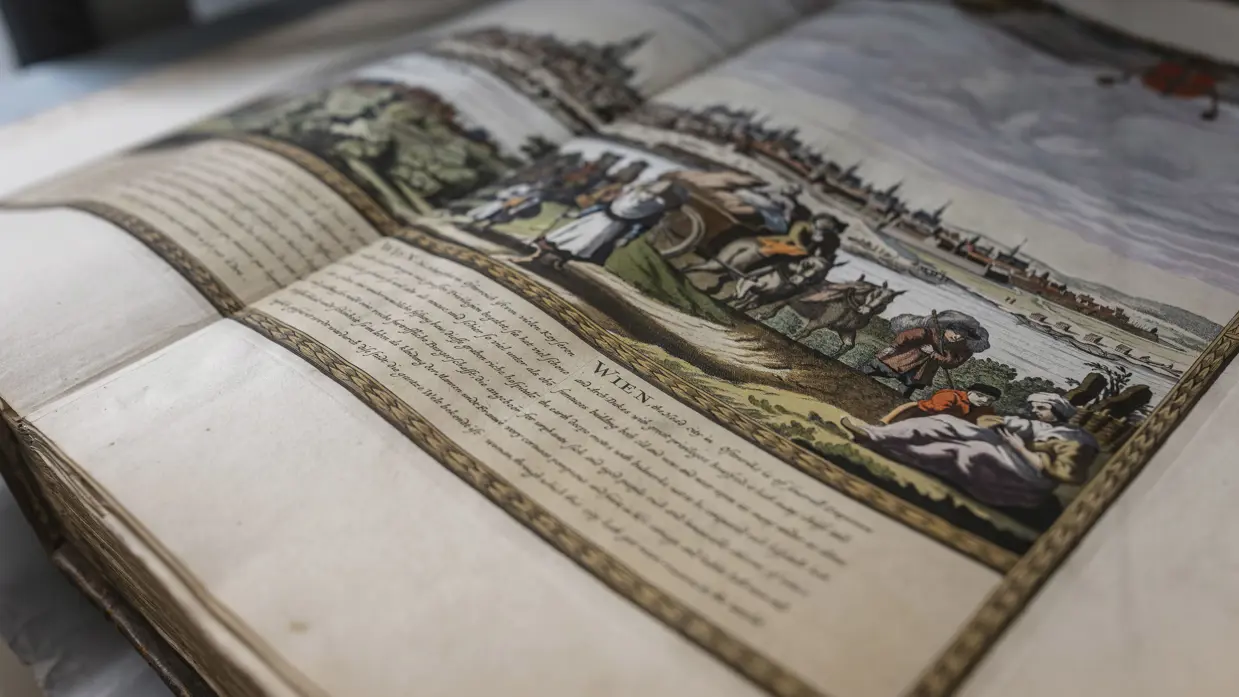 Een open, oud boek met een gekleurde tekening van een landschap, mensen, paarden en een kar, en geschreven tekst ernaast.