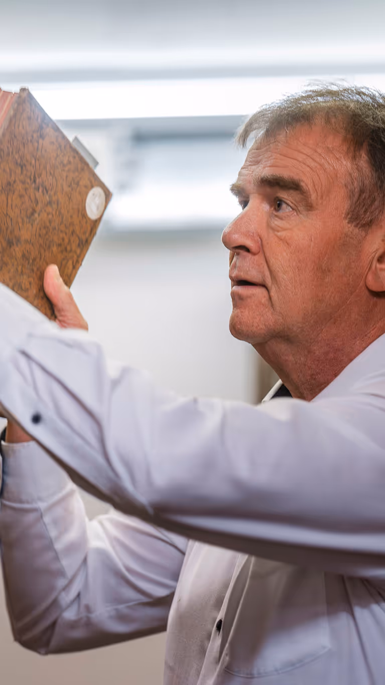 Een man in een wit overhemd pakt een oud, bruin boek van een plank vol oude boeken in een bibliotheek.