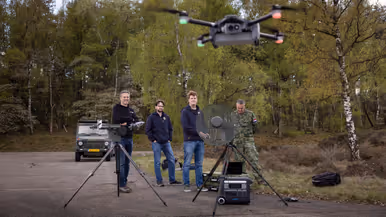 Personeel staat bij de Tracking Antenna Rotator terwijl een drone op de voorgrond hovert. 