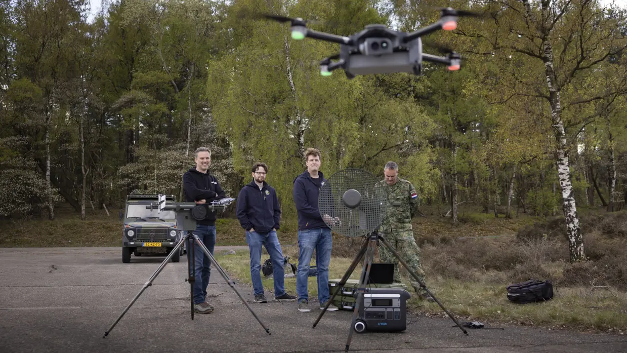 Personeel staat bij de Tracking Antenna Rotator terwijl een drone op de voorgrond hovert. 