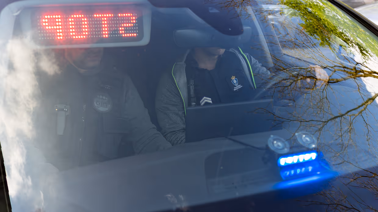 Twee Nederlandse marechaussees zitten in burger in een onopvallende auto, gezien door de voorruit.