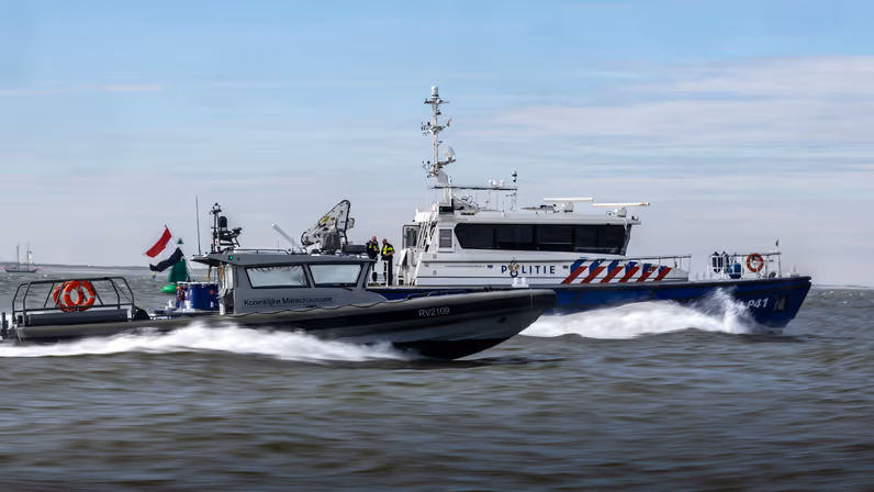 Een politieboot en een rhib-boot van de Koninklijke Marechaussee varen zij aan zij.