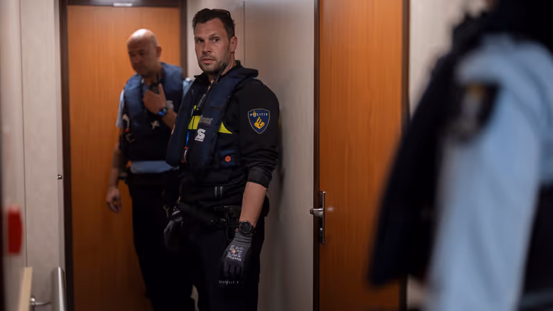 Een marechaussee en een politieman staan in een hal tegenover aan andere marechaussee.