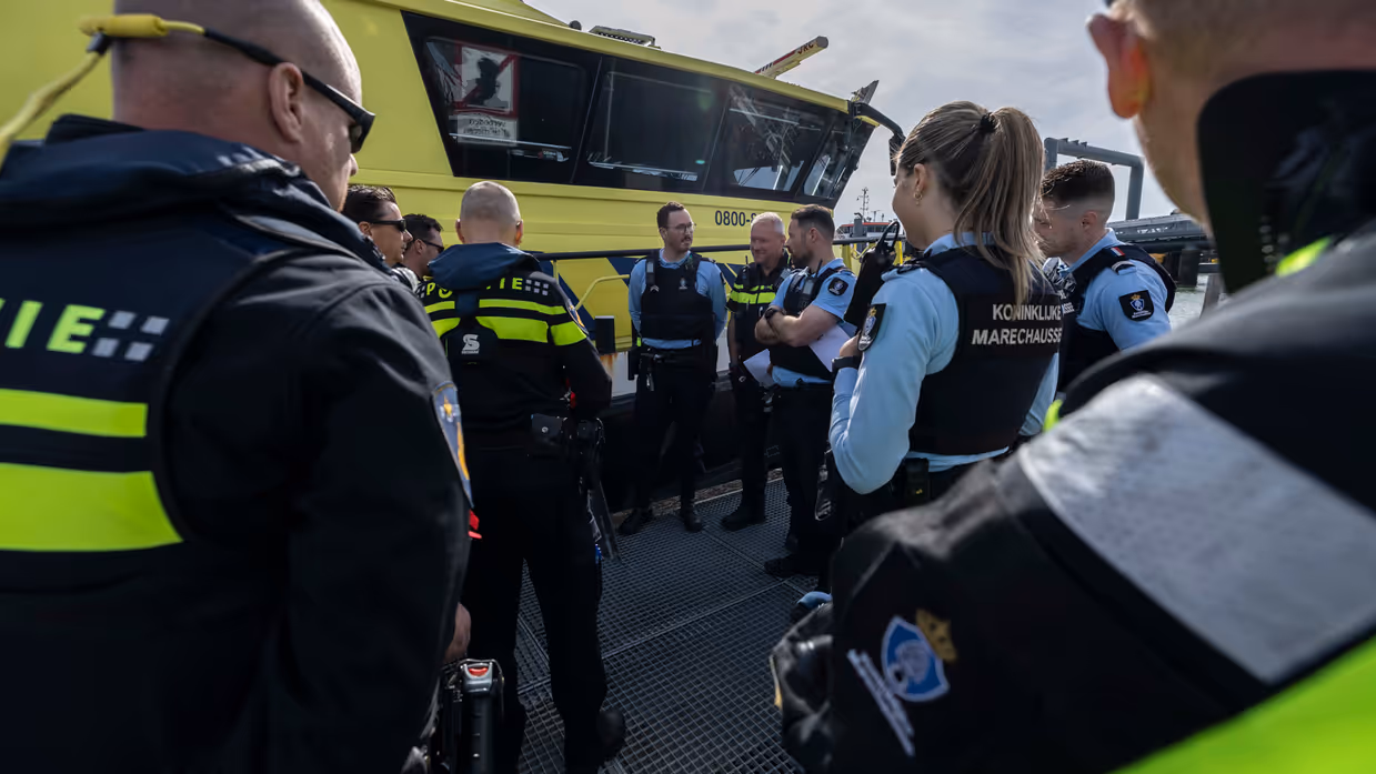 Marechaussees en politiemensen praten met elkaar op het dek van een schip.