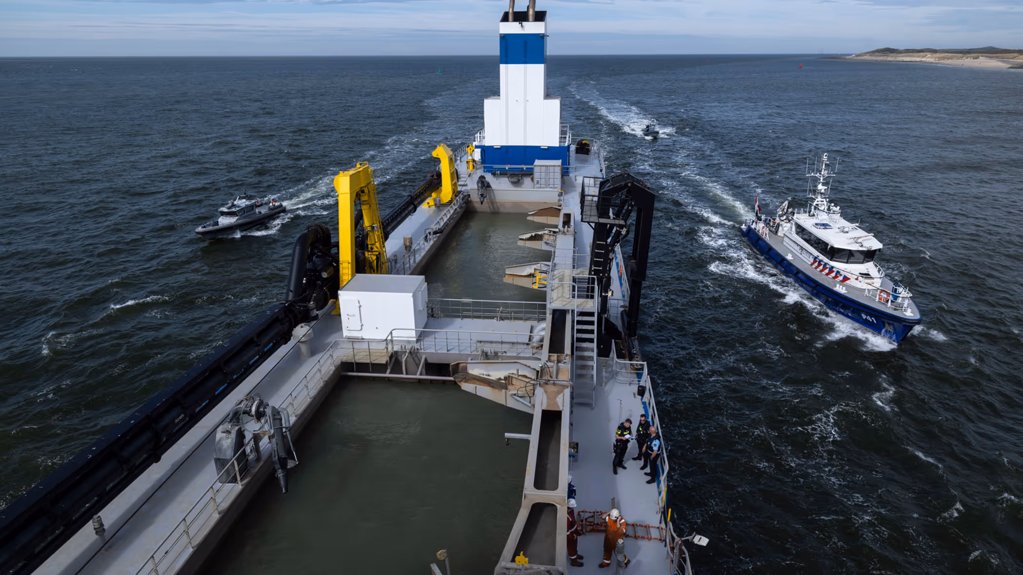Een politieboot en een rhib-boot van de Koninklijke Marechaussee flankeren een groot schip.